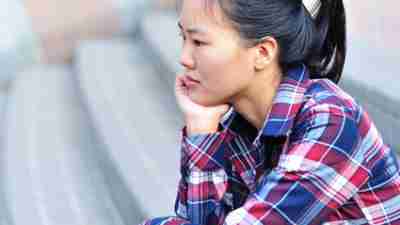 Profile of teen girl, with her chin in her hands, looking worried
