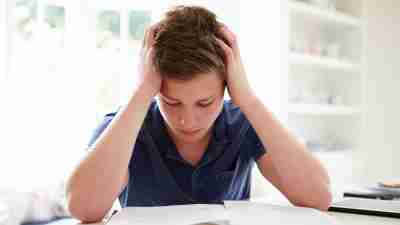 A teenage boy reading with his hands at either side of his head.