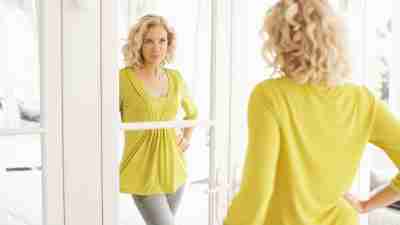 An older woman with ADHD looks at herself in a mirror skeptically, representing eating disorders in older women.