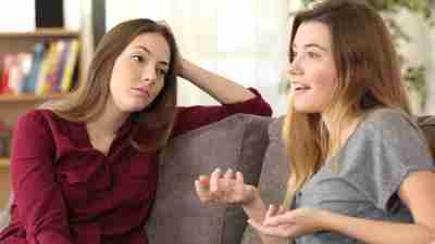 Bored girl listening to her emotionally draining friend having a conversation sitting on a couch in the living room at home.