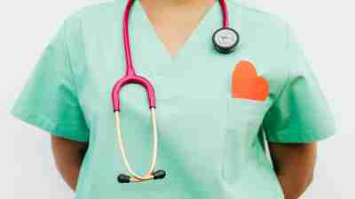 Heart Disease in Women is common, and overlooked. Photo shows woman in scrubs with stethoscope around her neck and paper heart in breast pocket.