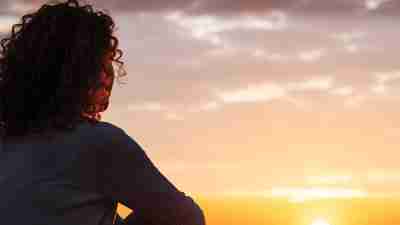 Women, pictured from behind, stares at the sunset, communicating the pain of intimate partner violence.