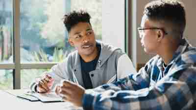 male teen sitting at desk talking cheerfully with another male student