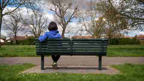 ADHD Woman sitting on bench with back turned looking at the park thinking