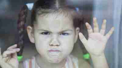 Little girl with ADHD angrily pressing face against glass door