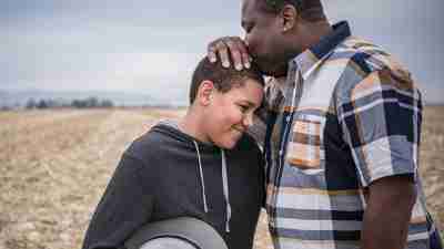 A Black father kisses the head of his young son, representing the power of Behavioral Parent Training (BPT) for ADHD families