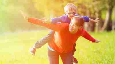 Son with ADHD on mother's back outside with arms spread out as part of game